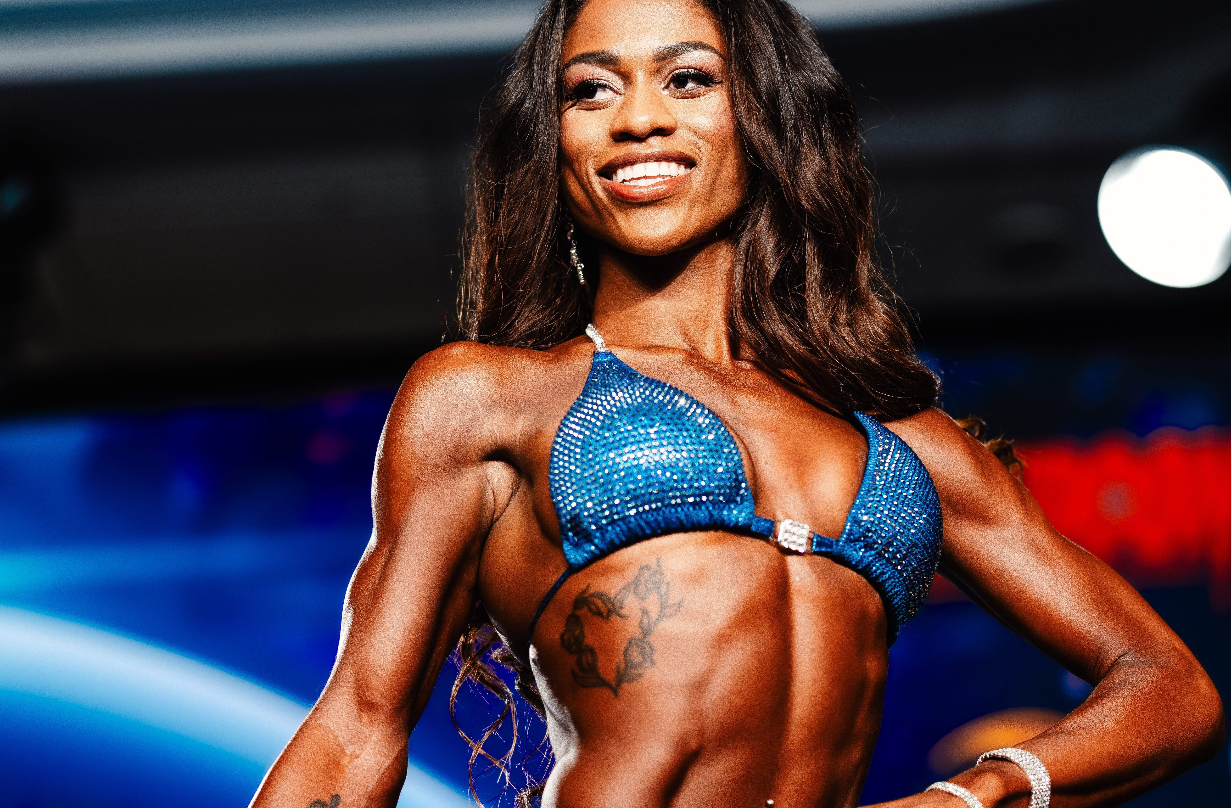 Alexandria Grace in a powerful competition pose on the IFBB stage under dramatic lighting